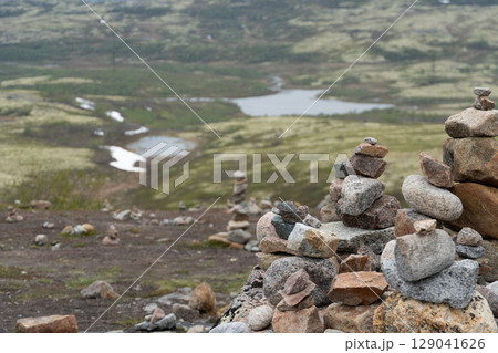 Stone cairns stacked on the tundra overlook a winding river and moss-covered hills near Teriberka, Russia 129041626