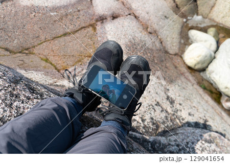 Close-up of hikers legs on rocky ground with smartphone placed on shoes reflecting a selfie 129041654