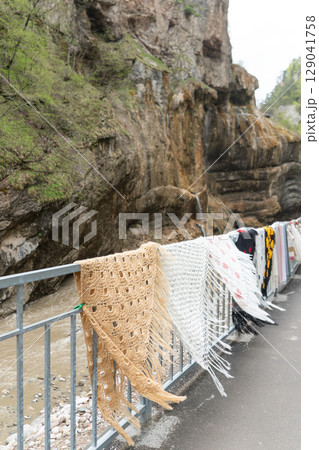 Colorful handwoven shawls and scarves displayed along a metal railing in the scenic Chegem Gorge, Kabardino-Balkaria, Russia 129041758
