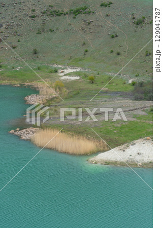 A vivid turquoise mountain lake winds through the lush, mist-covered hills of the North Caucasus A vivid turquoise mountain lake winds through the lush, mist-covered hills of the North Caucasus 129041787