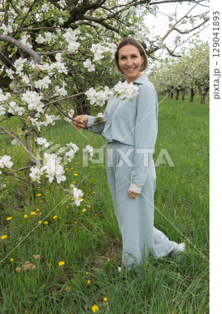 Middle-aged woman in soft blue loungewear standing among blooming apple trees. Wellness retreats, organic skincare, spring fashion, and mental health campaigns can all benefit from this serene Middle-aged woman in soft blue loungewear standing among blooming apple trees. Wellness retreats, organic skincare, spring fashion, and mental health campaigns can all benefit from this serene 129041893