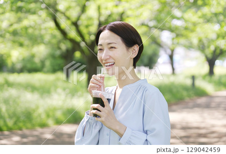 屋外でアイスコーヒーを飲む40代女性 129042459
