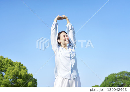 屋外で伸びをする女性 129042468