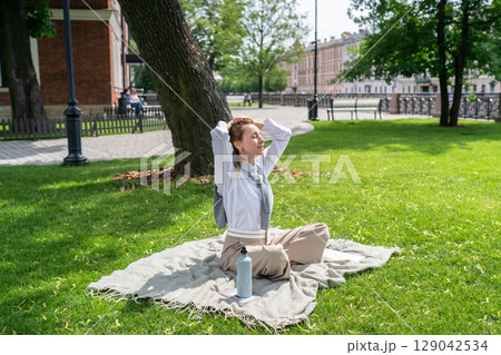 Calm woman open face to sun while sitting on lawn in sunny summer park, sun protection, UV heat 129042534