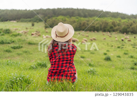 A woman wearing a straw hat sits in a field of grass 129043835