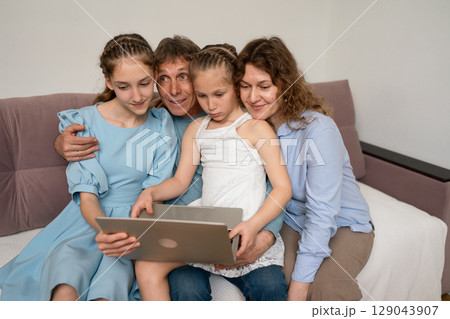Family laptop couch: Parents and daughters enjoy screen at home today. Family laptop couch: Parents and daughters enjoy screen at home today. 129043907
