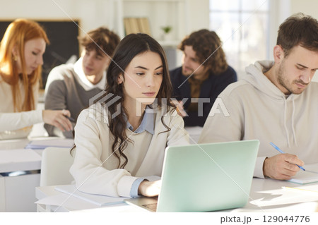Students group working and study at laptop online at desk in college class, trainee interns sitting Students group working and study at laptop online at desk in college class, trainee interns sitting 129044776