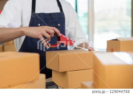 E-commerce Packaging. Worker sealing boxes with tape for shipping in a modern workspace. E-commerce Packaging. Worker sealing boxes with tape for shipping in a modern workspace. 129044788