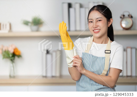 Preparing for Cleaning. Young woman putting on rubber gloves with a smile. 129045333