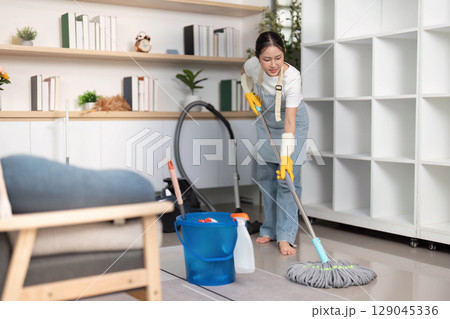 Home Cleaning. Young woman mopping floors while maintaining a clean and organized home environment. Home Cleaning. Young woman mopping floors while maintaining a clean and organized home environment. 129045336
