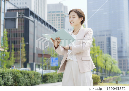 オフィス街で手帳を持って立つ若いビジネスウーマンのポートレート オフィス街で手帳を持って立つ若いビジネスウーマンのポートレート 129045872