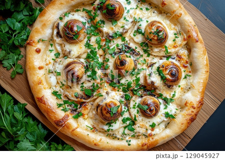 Overhead view of a gourmet pizza topped with escargot, featuring melted cheese, garlic, and herbs, displayed on a wooden board with fresh parsley in soft evening light 129045927