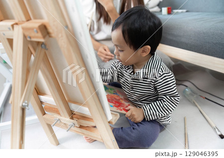 Artistic expression. Child focused on painting with guidance from mother. Artistic expression. Child focused on painting with guidance from mother. 129046395