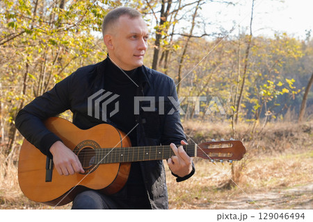 Blonde man playing string guitar outdoors in autumn forest. Concept of sound therapy, mental health and wellness rituals. Calmness tranquility audio-sensory practices. Aura farming energy 129046494