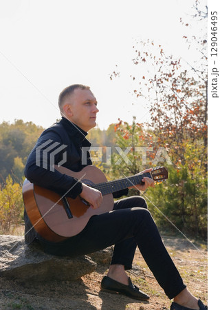 Portrait of smiling caucasian artist plays wooden acoustic guitar in autumnal park. Young songwriter plays string musical instrument hobby outside in nature fall time. Audio music healing 129046495