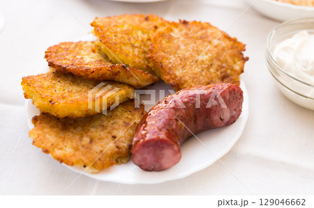 Fried grated potato pancakes with fried sausage on white plate 129046662