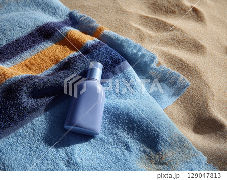 Light blue sunscreen bottle placed colorful beach towel sandy beach sunny weather relaxing summer scene skincare product for sun protection outdoor setting beach vacation travel essentials skin 129047813