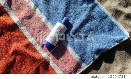 Bottle of sunscreen lotion beach towel with sand background sunny weather outdoor setting sun protection summer skin care hydration SPF beach travel outdoor activity skin protection sunblock 129047814