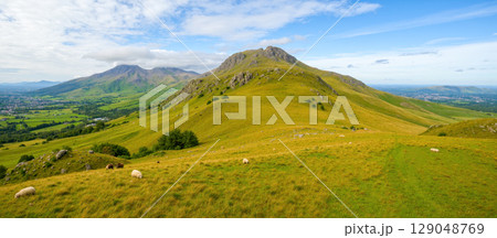 Stunning landscape with green hills and majestic mountain peaks in background under blue sky with clouds on sunny summer day Stunning landscape with green hills and majestic mountain peaks in background under blue sky with clouds on sunny summer day 129048769