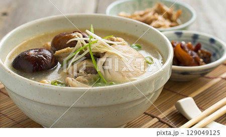 A bowl of chicken soup with mushrooms and garnish on a bamboo placemat near 129049125