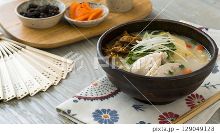 bowl of japanese chicken rice soup with pickles and a decorative fan nearby 129049128