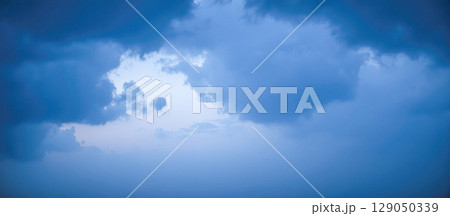Hole of clear light in dark blue stormy clouds, atmospheric sky background symbolizing hope, freedom, or wonderful new beginning Hole of clear light in dark blue stormy clouds, atmospheric sky background symbolizing hope, freedom, or wonderful new beginning 129050339