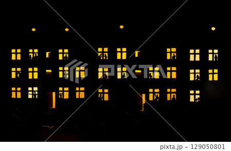 Quarantine. Residential building with silhouettes of people in the glowing windows. Quarantine. Residential building with silhouettes of people in the glowing windows. 129050801