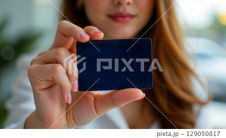 Woman holding blank black card with confident expression, showcasing card in close up shot with blurred background 129050817