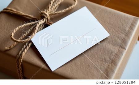 Blank white card on brown gift box tied with rustic twine bow, cozy and simple present concept for celebration or greeting 129051294