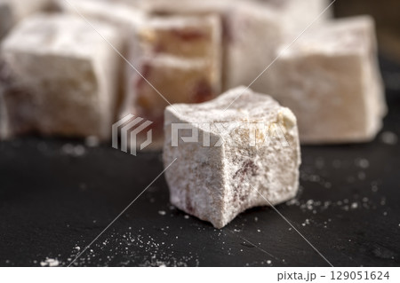 sweet lukum slices with cherry slices on a black board , cubes of sweet Turkish delight with the addition of dried red berries in powdered sugar sweet lukum slices with cherry slices on a black board , cubes of sweet Turkish delight with the addition of dried red berries in powdered sugar 129051624