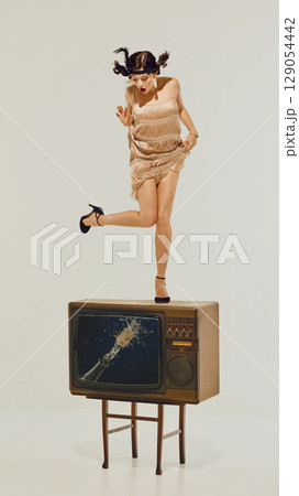 Woman in flapper dress standing shocked on retro TV with exploding champagne image on screen 129054442