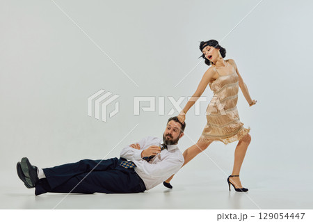 Woman in flapper dress dragging man by hair while he holds drink and lies on floor Woman in flapper dress dragging man by hair while he holds drink and lies on floor 129054447