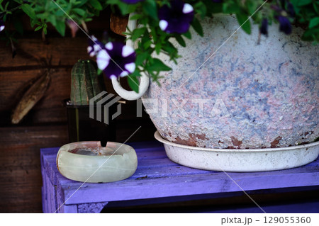 Floral arrangement with a weathered pot and a stone ashtray on a rustic purple table in a garden setting Floral arrangement with a weathered pot and a stone ashtray on a rustic purple table in a garden setting 129055360