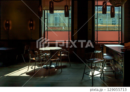 Table at a restaurant with sunlight streams through the Large windows, casting light and shadow patterns on the floor, wooden dining tables, chairs and the floor. Table at a restaurant with sunlight streams through the Large windows, casting light and shadow patterns on the floor, wooden dining tables, chairs and the floor. 129055713