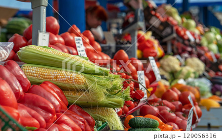 Cobs of corn among a huge selection of fresh vegetables on the counter of a food market. Selective focus on cobs of corn. 129056316