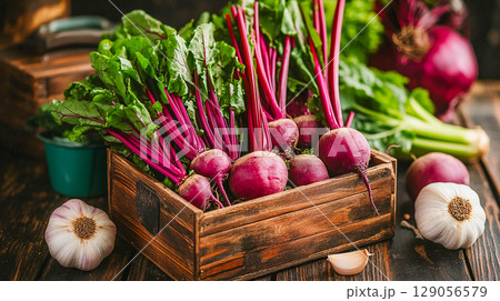 A wooden box filled with fresh beets with their tops. Garlic heads are lying around. A natural farmer's market.	 129056579