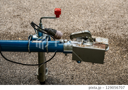 Trailer Hitch Coupling Mechanism On Paved Surface: Close-Up Of Metal Tow Bar With Brake Cable, Rubber Sleeve, And Mounting Hardware For Towing Connection 129056707