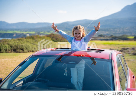 Little girl joyfully sticks out of car sunroof with raised hands against the backdrop of mountains in Northern Cyprus. The image symbolizes freedom, adventure, and the excitement of travel with child 129056756