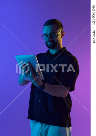 Man using tablet in contemporary purple-lit room focused on digital connectivity concept Man using tablet in contemporary purple-lit room focused on digital connectivity concept 129056846