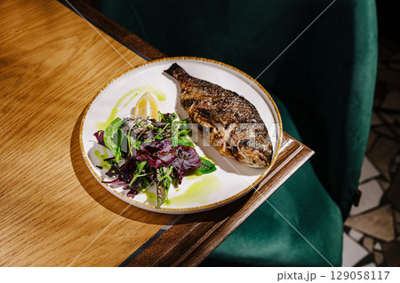Grilled fish with fresh salad served on a white plate in a cozy restaurant 129058117