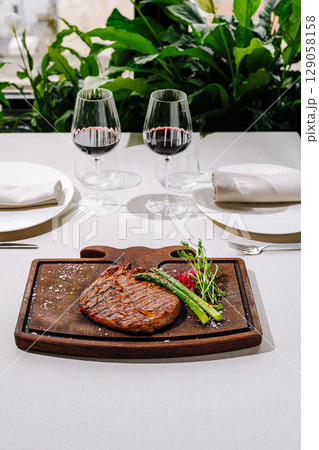 Elegant dining setup featuring steak and wine in a lush environment Elegant dining setup featuring steak and wine in a lush environment 129058158