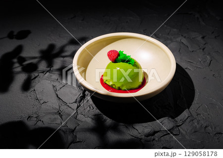 Green dessert with berry garnish served in elegant bowl on dark surface 129058178