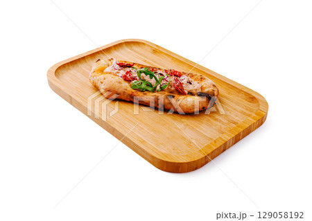 Freshly baked flatbread topped with herbs and red vegetables on wooden tray 129058192