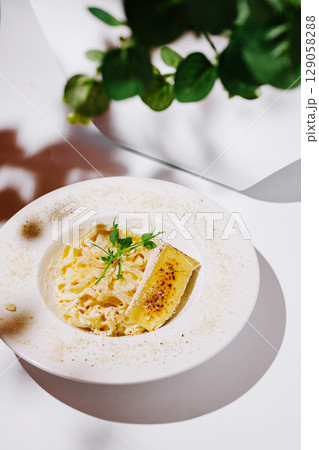 A sophisticated plate of creamy fettuccine pasta elegantly garnished with microgreens and a slice of bruleed cheese, presented on a white ceramic dish with parmesan dusting A sophisticated plate of creamy fettuccine pasta elegantly garnished with microgreens and a slice of bruleed cheese, presented on a white ceramic dish with parmesan dusting 129058288
