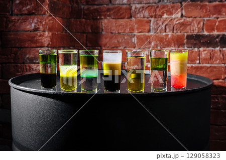Creative shot glasses lined up on a bar counter with colorful liquids Creative shot glasses lined up on a bar counter with colorful liquids 129058323