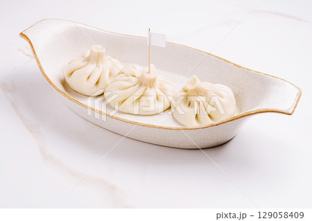 Three traditional Georgian khinkali dumplings arranged in a cream-colored ceramic dish 129058409