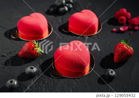 Red heart-shaped desserts with fresh berries on dark slate background 129058432