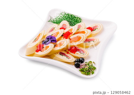 An elegant appetizer featuring thin pancake rolls filled with smoked salmon, cream cheese, and herbs, topped with red caviar and garnished with edible flowers, blueberries, and microgreens 129058462