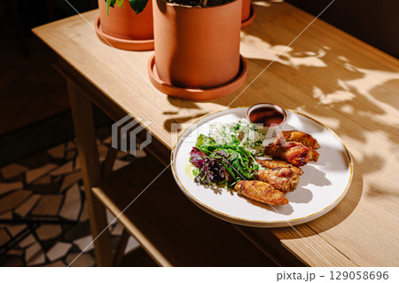 Delicious chicken wings served with fresh salad and rice on wooden table 129058696