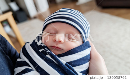 Newborn baby wrapped in soft blanket held in arms, featuring cozy home setting 129058761